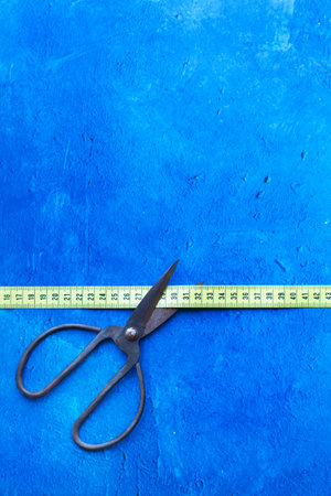 Scissors with large handles cutting a measuring tape on a blue background with copy spaceの写真素材