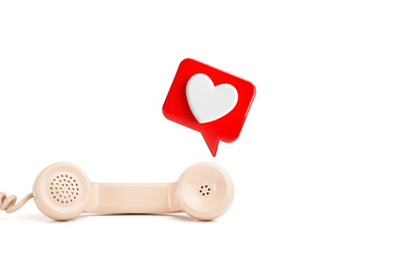 A telephone handset with a red speech bubble with a white heart inside on a white background with...