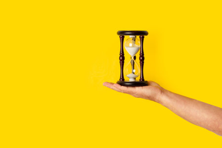 Man hand holding an hourglass on a yellow background with copy spaceの写真素材