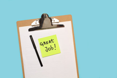Great job handwritten on a sticky paper on a clipboard table with white paper sheets on a light blue backgroundの写真素材