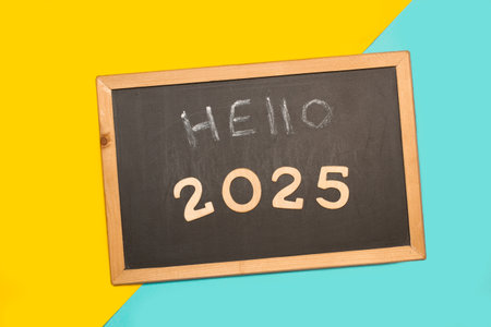 Hello 2025 short phrase on a blackboard on a light blue and yellow backgroundの写真素材