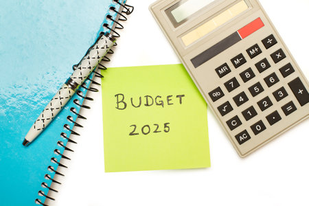 A note pad, a pen, a calculator and a yellow paper with 2025 budget phrase written on it on a white backgroundの写真素材