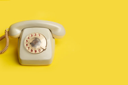 A vintage dial telephone on a yellow background with copy space