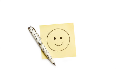 A smiley face drawn on a yellow sticky paper and a pen on a white background with copy spaceの写真素材