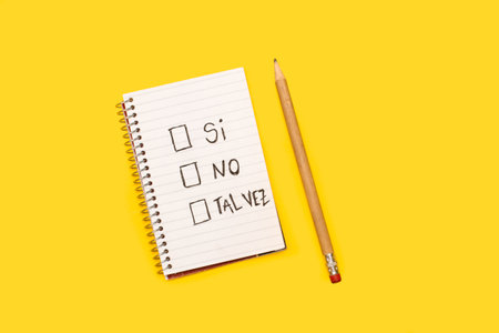A spiral notepad with the words si, no, and perhaps and squares spaces to choose from and a pencil on a yellow background (trad, yes, no, maybe)の写真素材