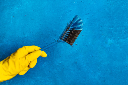 A hand wearing a yellow cleaning glove holding a cleaning brush on a blue background with copy spaceの写真素材
