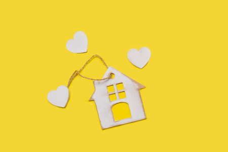 A white wooden toy house and three white hearts on a yellow background with copy spaceの写真素材