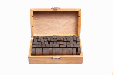 Stamps with capital letters and numbers in a wooden box on a white background with copy space