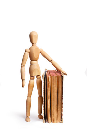 A wooden mannequin standing close to a book isolated on a white backgroundの写真素材
