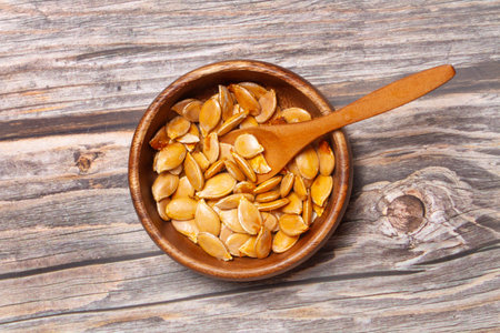 Pumpkin seeds in a wooden bowl with a wooden spoon on a wooden table in a top viewの写真素材