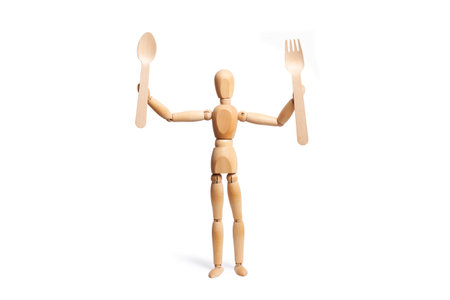 A wooden toy mannequin holding a fork and a spoon on white backgroundの写真素材