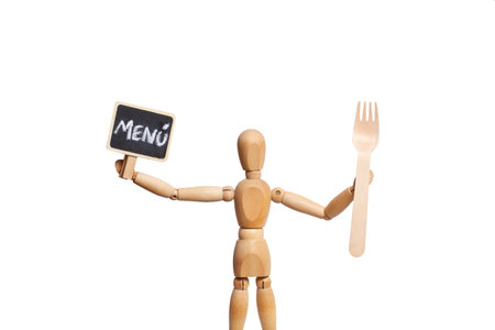 A wooden toy mannequin holding a fork and a menu banner on white backgroundの写真素材