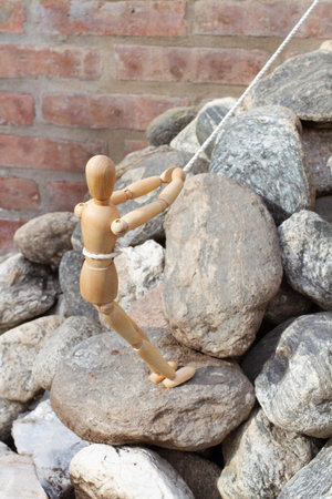 A wooden mannequin standing holding a rope and climbing rocks