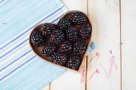 fresh organic blackberries in hearth style shape basket  on white background retro kitchen table and blue kitchen clothの写真素材