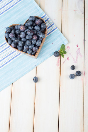 fresh organic blueberries in heart style shape basket and blue kitchen cloth on white background retro kitchen tableの写真素材