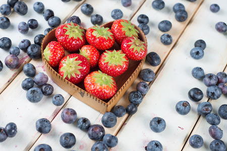fresh organic strawberries and blueberries in hearth style shape basket  on white background retro kitchen tableの写真素材