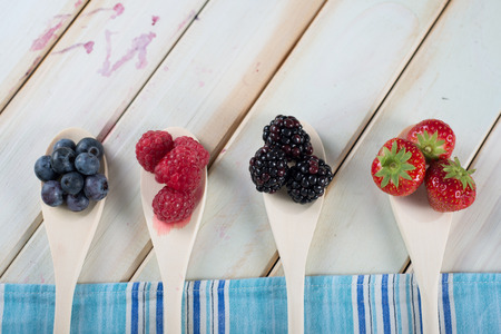fresh organic berrys fruits on wooden spoon over blue kitchen cloth on white background retro style wooden tableの写真素材