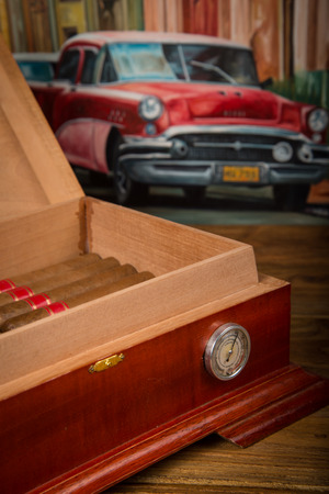 Cuban cigars and humidor on rustic wooden table with Cuban painting of american old car in backgroundの写真素材