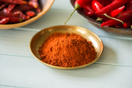 chilli powder in bowl with dried and fresh peppers in background on white wood tableの写真素材