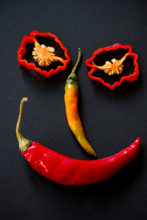 Smiling funny face made with hot chilli peppers on black slate backgroundの写真素材