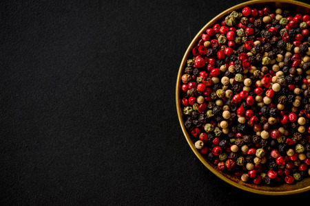 colorful pepper seeds in golden cooper bowl on black slate backgroundの写真素材