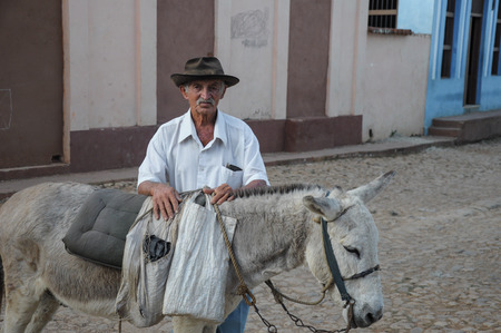 TRINIDAD, CUBA - DECEMBER 28, 2013: Old local man present donkey on street in Trinidad, Cuba. Donkeys are use as taxi for tourist in this UNESCO listed city.のeditorial素材