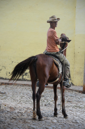 TRINIDAD, CUBA - JANUARY 28, 2013 Cuban local man sitting on horse  and posing to photos  on street in UNESCO protected city of Trinidad, Cuba.のeditorial素材