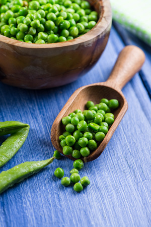 Wooden scoop with fresh peas on blue tableの写真素材