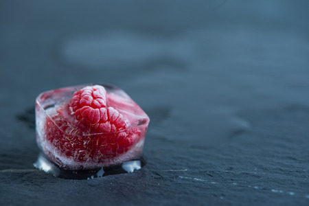 Frozen rasberries in ice cube on slate backgroundの写真素材