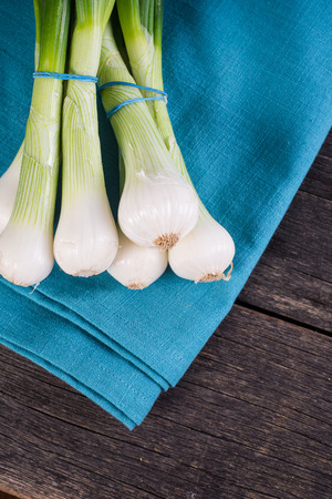 Fresh bunch of spring onion on cloth on wooden tableの写真素材