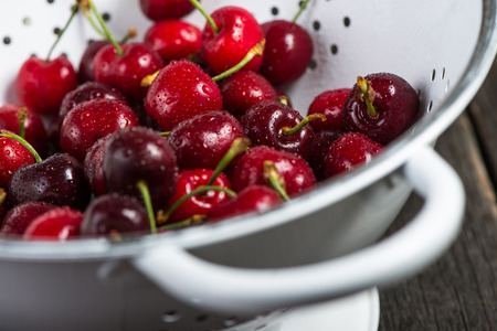 Fresh clean organic ripe cherries in vintage colander, on rustic wooden tableの写真素材