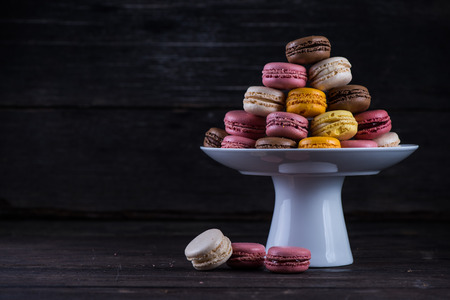 Stack of vibrant fresh macaroons on platter and wooden rustic backgroundの写真素材