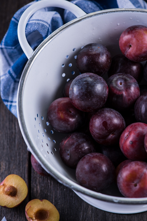 Fresh plums in rustic colander on wooden tableの写真素材