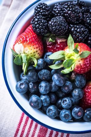 Rustic bowl full of forest summer berry fruits, from above on kitchen table.の写真素材