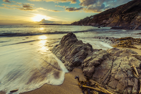 Filtered effect vintage photo, sunset at beach. Water flowing in slow motion, rocky shore and golden...