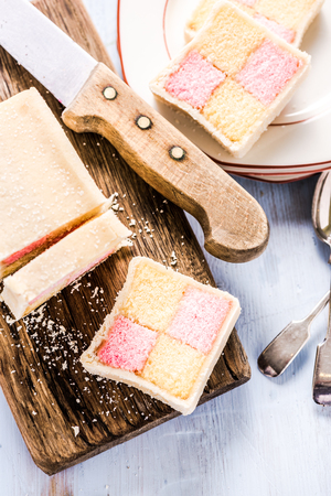 slicing Battenberg homemade sponge cake, on wooden boardの写真素材