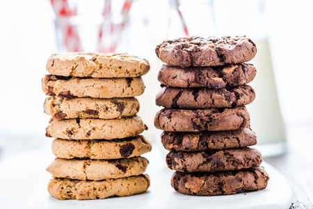 Stack of brown and chocolate cookies, milk in backgroundの写真素材