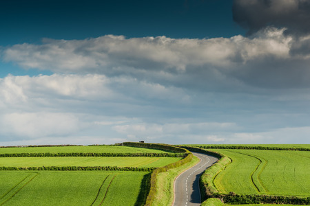 Rural road on rolling hills in countryside, cloudy sky.の写真素材