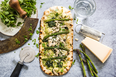 Pizza with fresh spring vegetables and herbs, from overhead on slate background