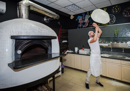 Bearded pizza chef play with pizza dough in traditional restaurantの写真素材