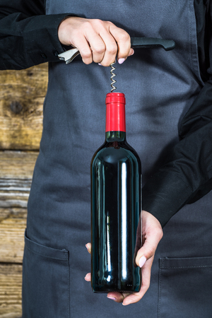 waitress in apron with corkscrew and red wine bottleの写真素材