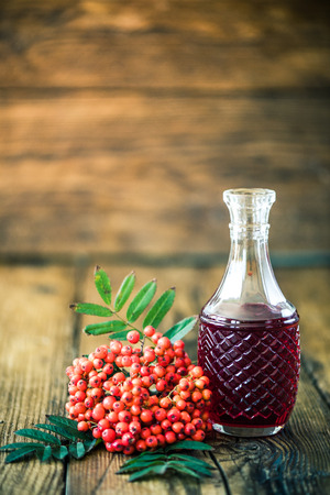 Rowanberry tincture vodka on wooden table with ashberry fruitsの写真素材