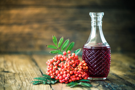 Rowanberry tincture vodka on wooden table with ashberry fruitsの写真素材