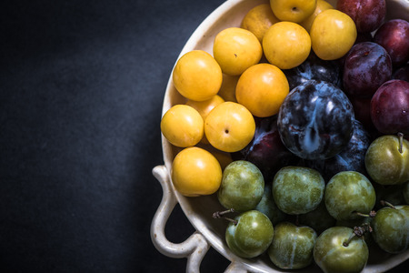 vibrant and ripe plums in bowl from local marketの写真素材