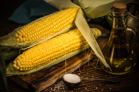 Whole corn on the cob on wooden board, dark moody imageの写真素材