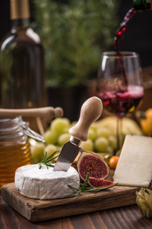 Pouring red wine into glass and serving with camembert.の写真素材