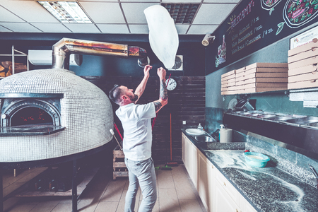 Bearded pizzaiolo chef lunching dough into air.