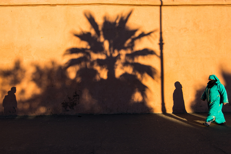 Marrakech,Morocco - January 2018:Muslim woman past by wall full of shadows in traditional clothes.のeditorial素材