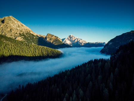 Morning fog over forest in Italian Dolomites mountains, aerial drone view.の写真素材