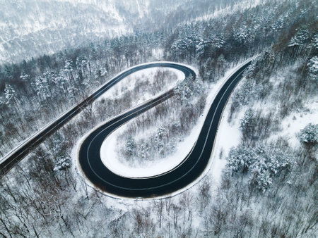 Curvy Windy Road in Snow Covered Forest, Top Down Aerial Drone View.